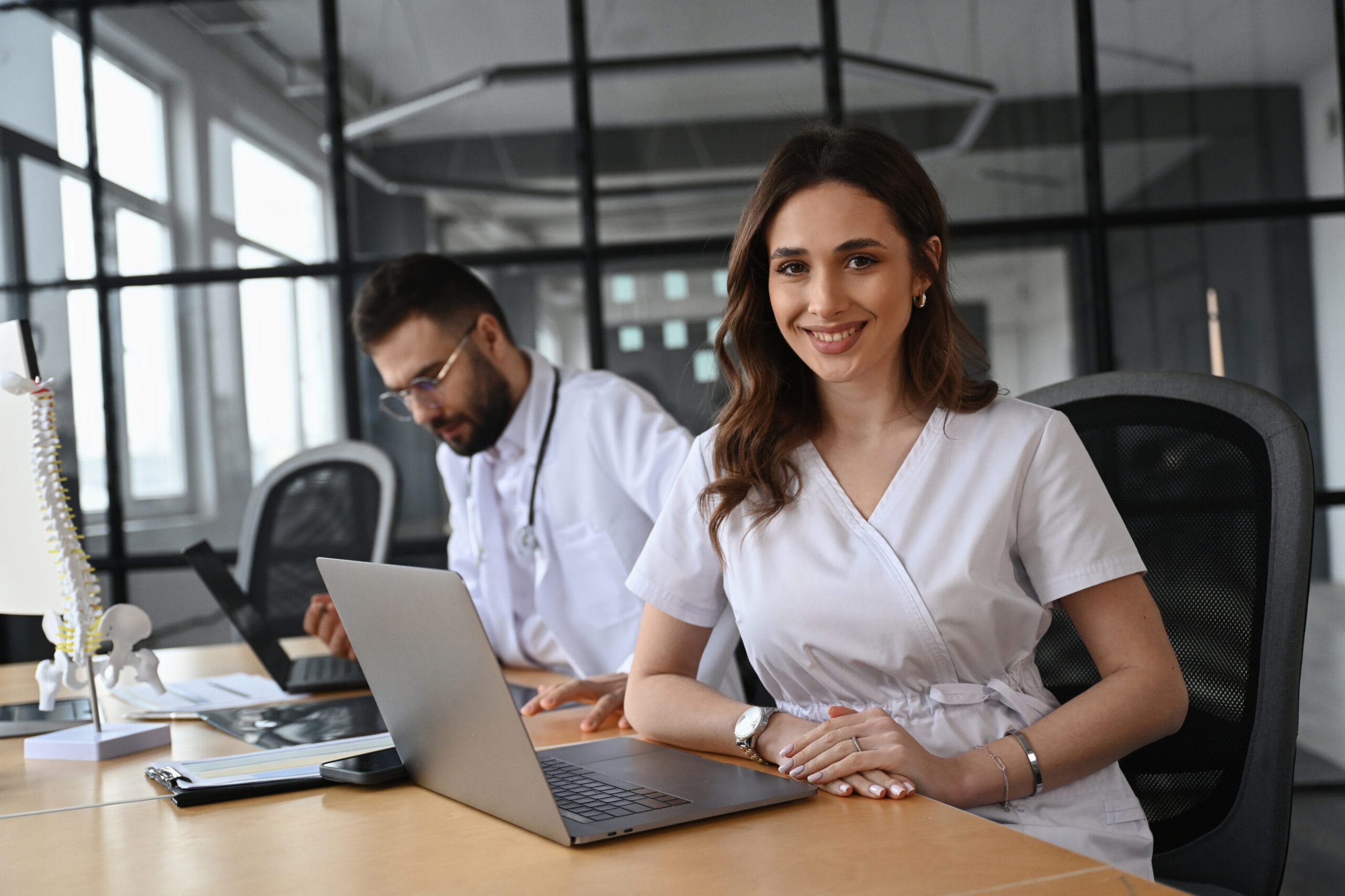 Médecin souriante travaillant sur ordinateur portable aux côtés d'un confrère en cabinet
